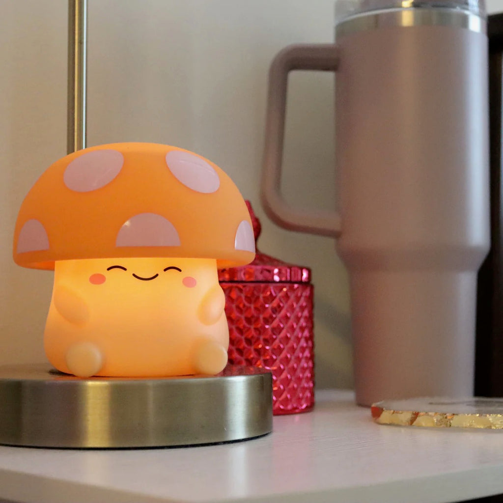Mushi mushroom night light glowing warm on a cozy desk beside a tumbler and candle