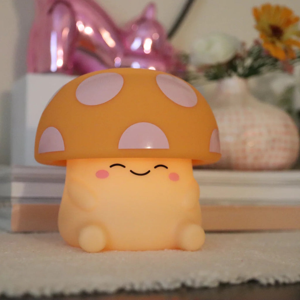 Mushi mushroom night light with a pink-spotted cap and smiling blushing face on a cozy styled shelf