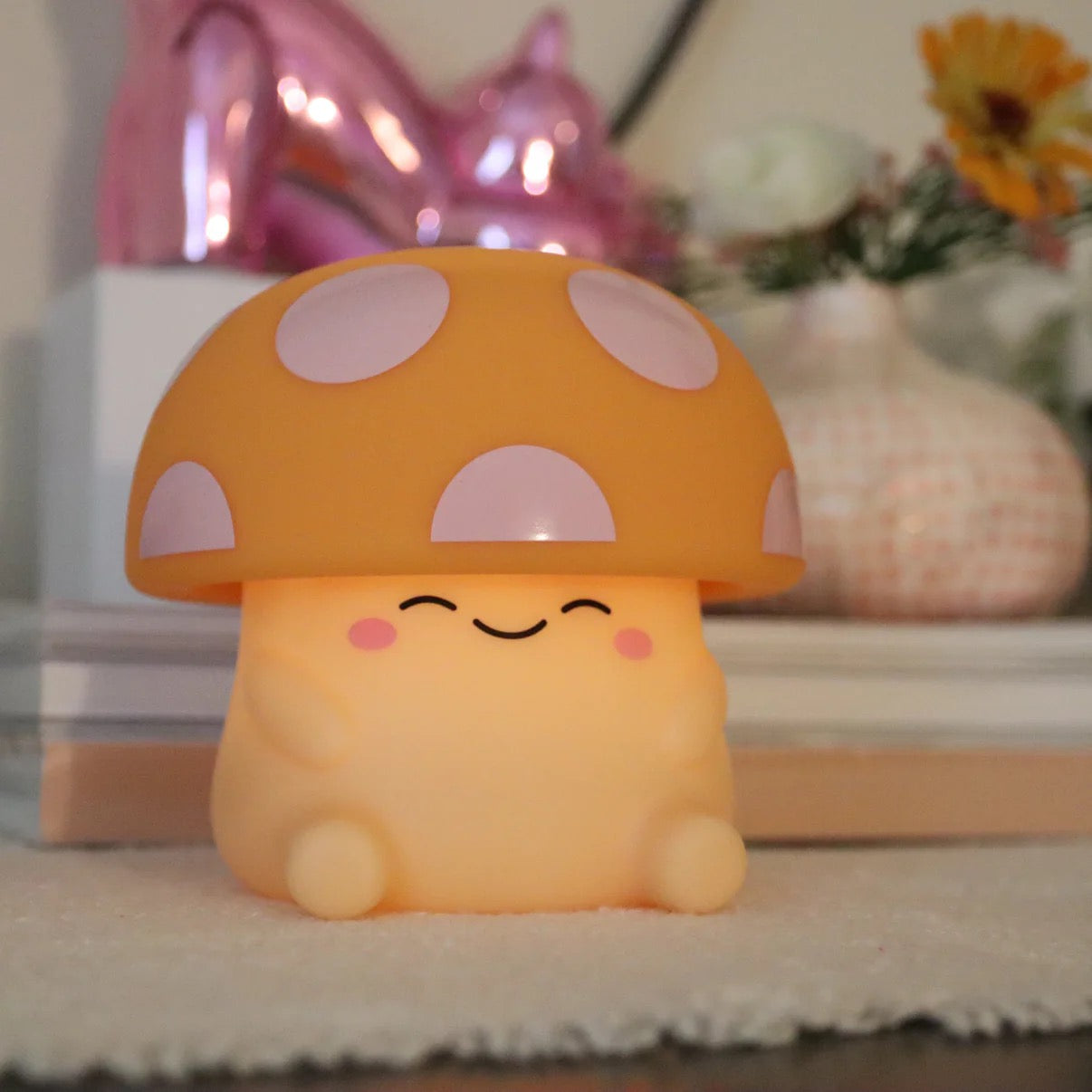Mushi mushroom night light with a pink-spotted cap and smiling blushing face on a cozy styled shelf