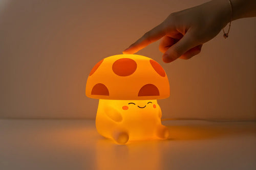 Mushi mushroom night light glowing warm orange while a hand taps the top to adjust the brightness